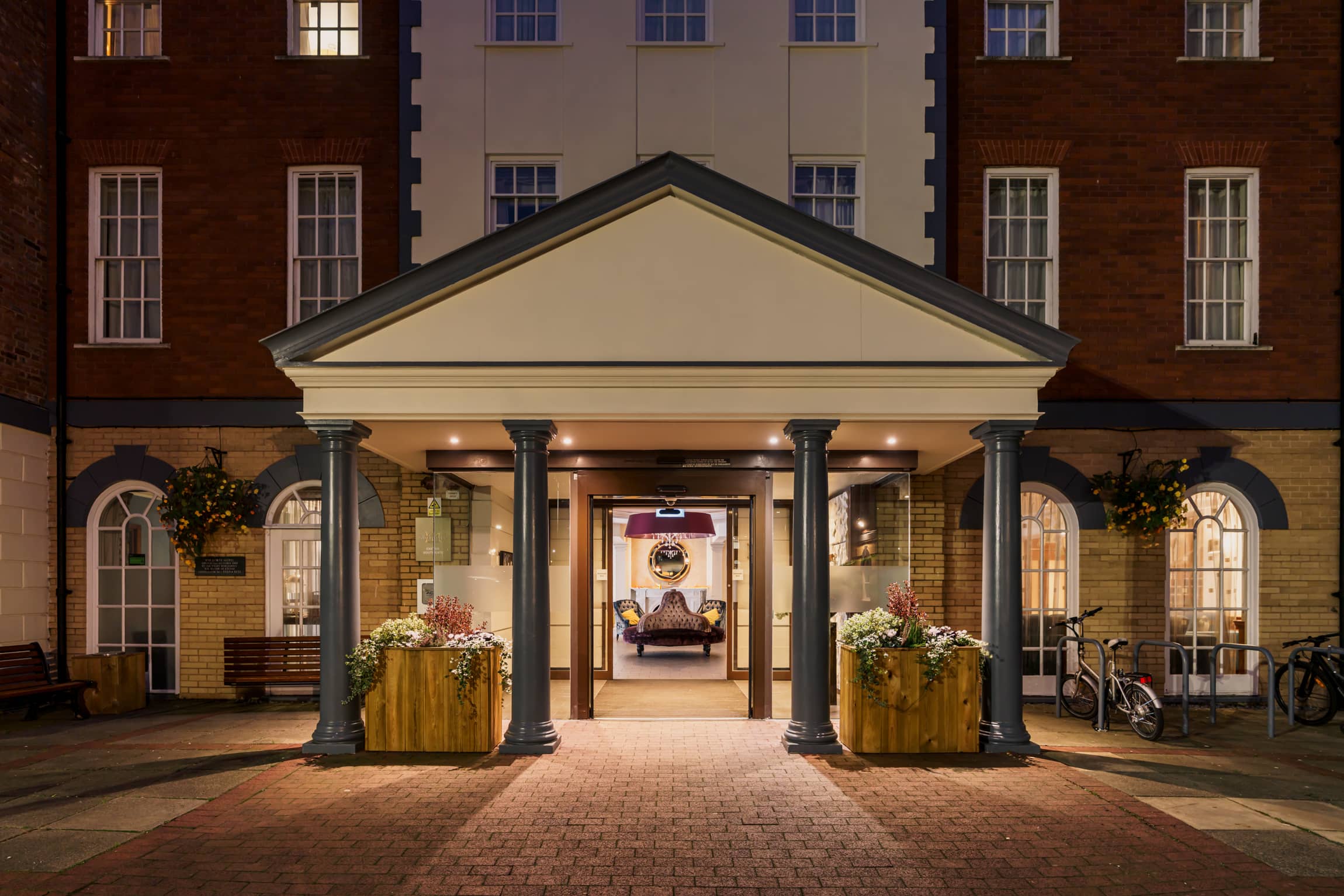 Illuminated hotel entrance with classical columns and flower planters at night