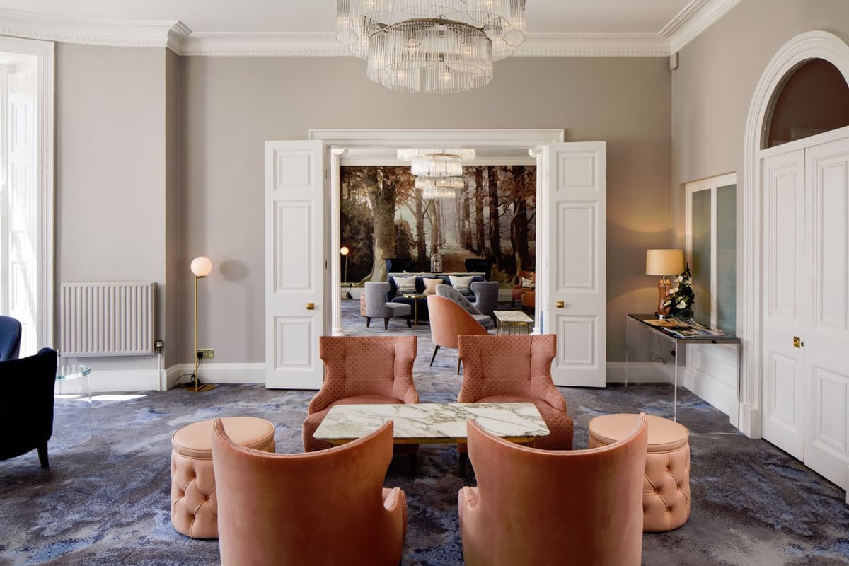 Elegant hotel lounge with blush velvet chairs, marble coffee table and tiered glass chandelier.