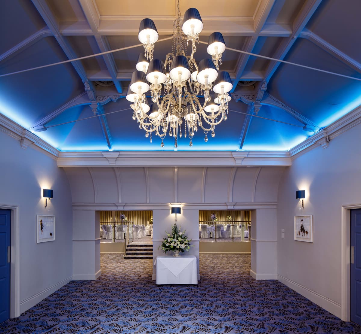 Grand function room with crystal chandelier, blue uplighting and patterned carpet at Bowden Hall.