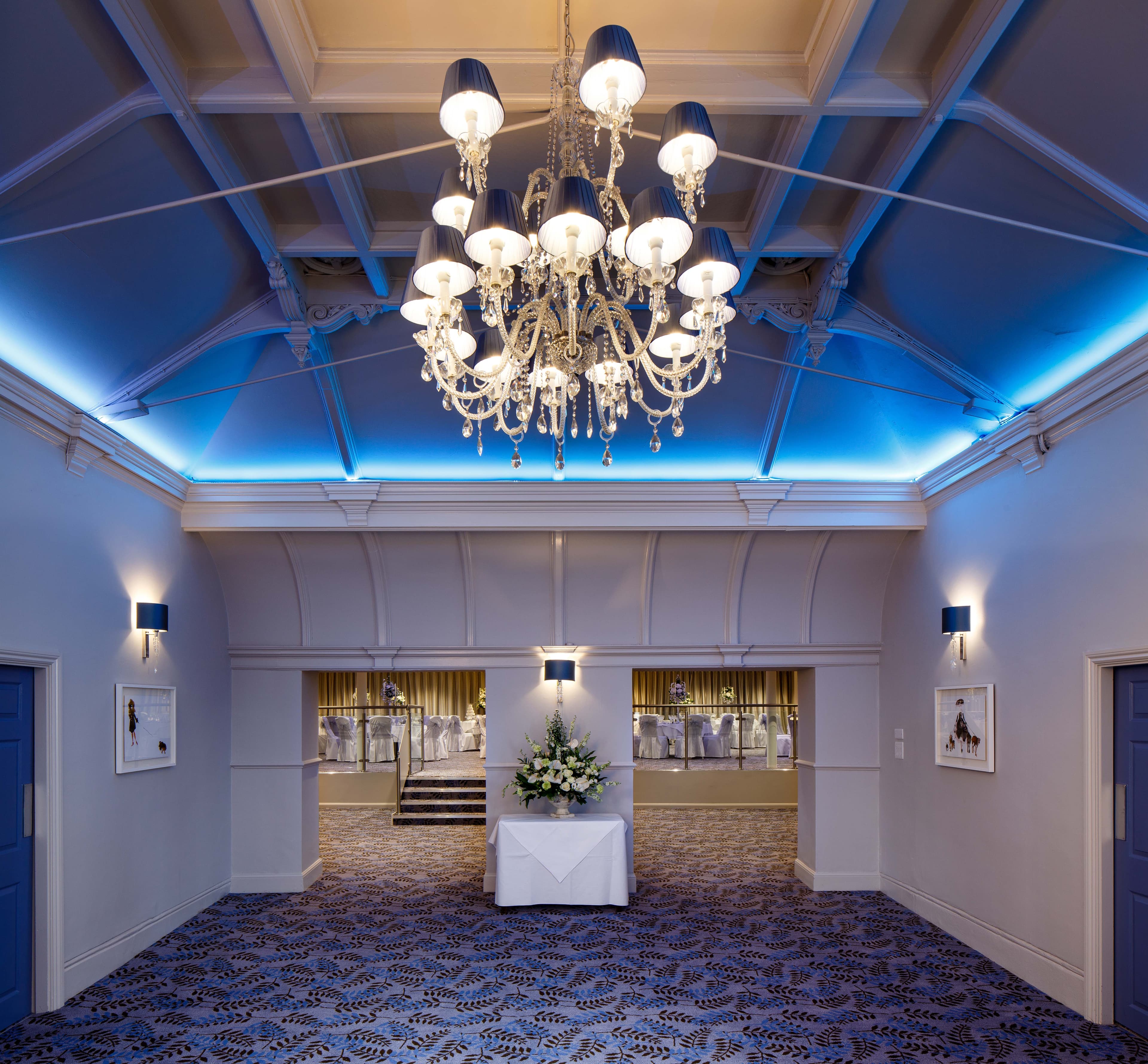 Grand function room with crystal chandelier, blue uplighting and patterned carpet at Bowden Hall.