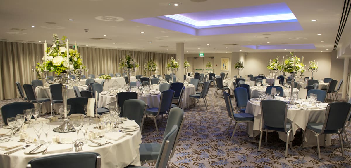 Banqueting suite laid for a formal dinner with tall floral centrepieces and blue uplighting