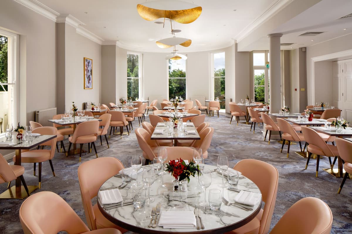 Bright hotel dining room with marble tables, blush chairs and gold ceiling lights.