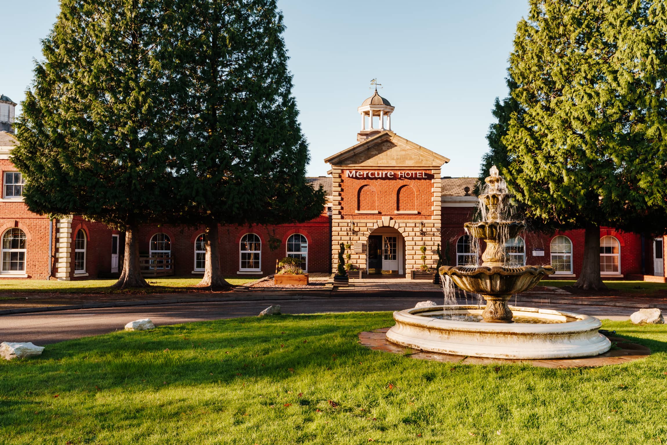 The red brick exterior of Mercure Haydock Park Hotel with a stone fountain and lawns.