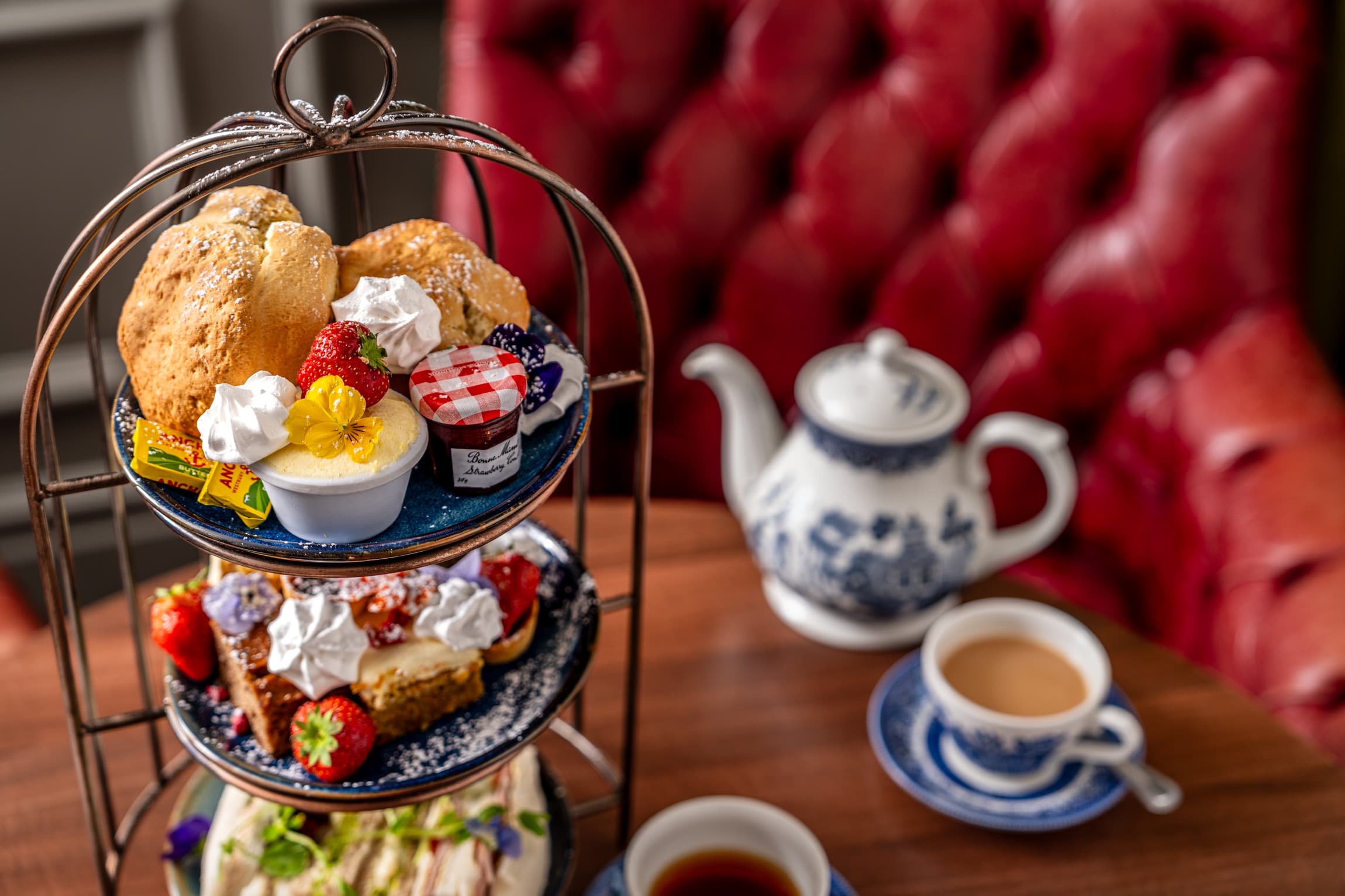Afternoon tea stand with scones, clotted cream and strawberries beside a blue and white teapot.