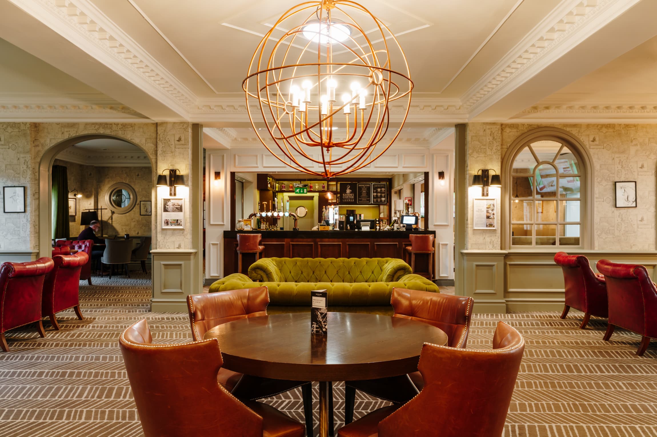 Hotel lounge bar with tan leather chairs, olive Chesterfield sofa and copper globe chandelier.