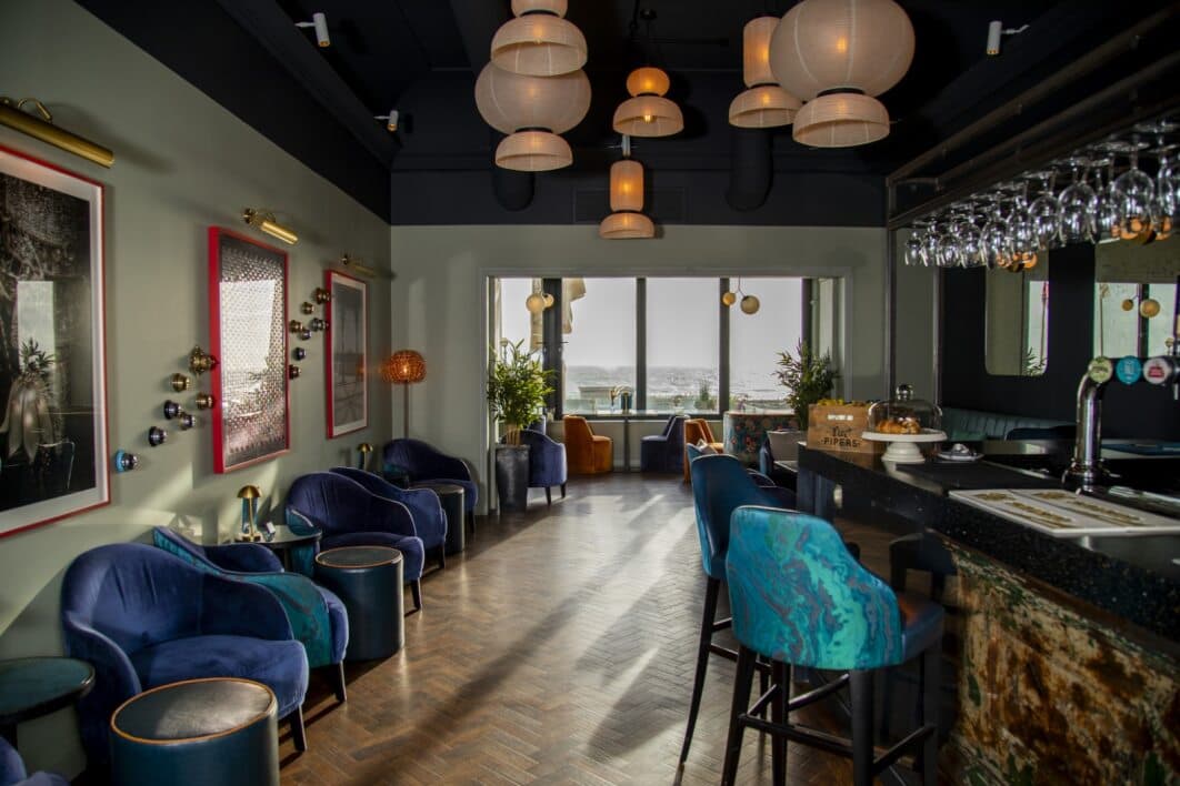 Stylish hotel bar with velvet armchairs, pendant lights and a sea view window.