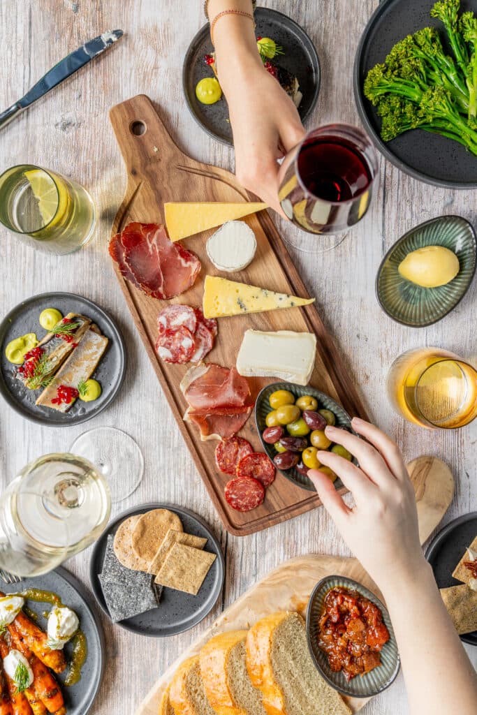 Overhead view of a charcuterie board with cheese, cured meats, olives and wine glasses.