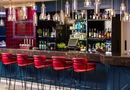 Stylish hotel bar with red velvet stools, dark marble counter and pendant lighting.