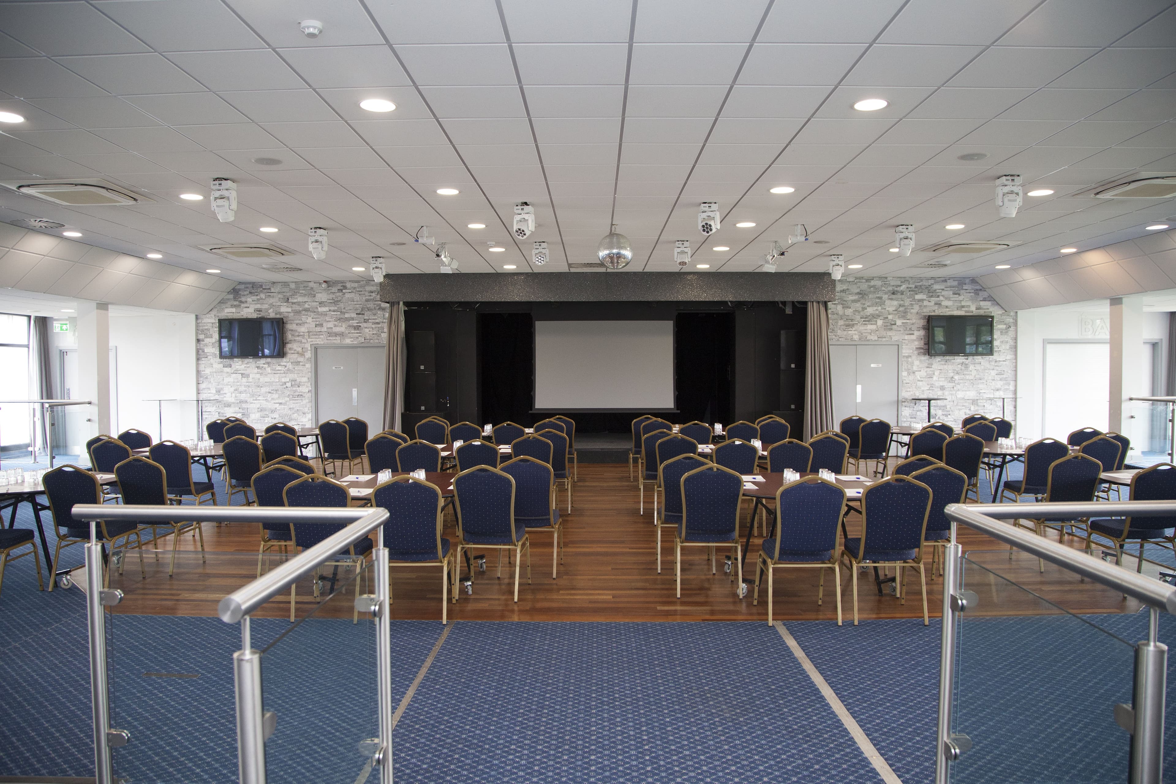 Conference room at Metropolitan Bushey set with banquet chairs, tables and a projection screen.
