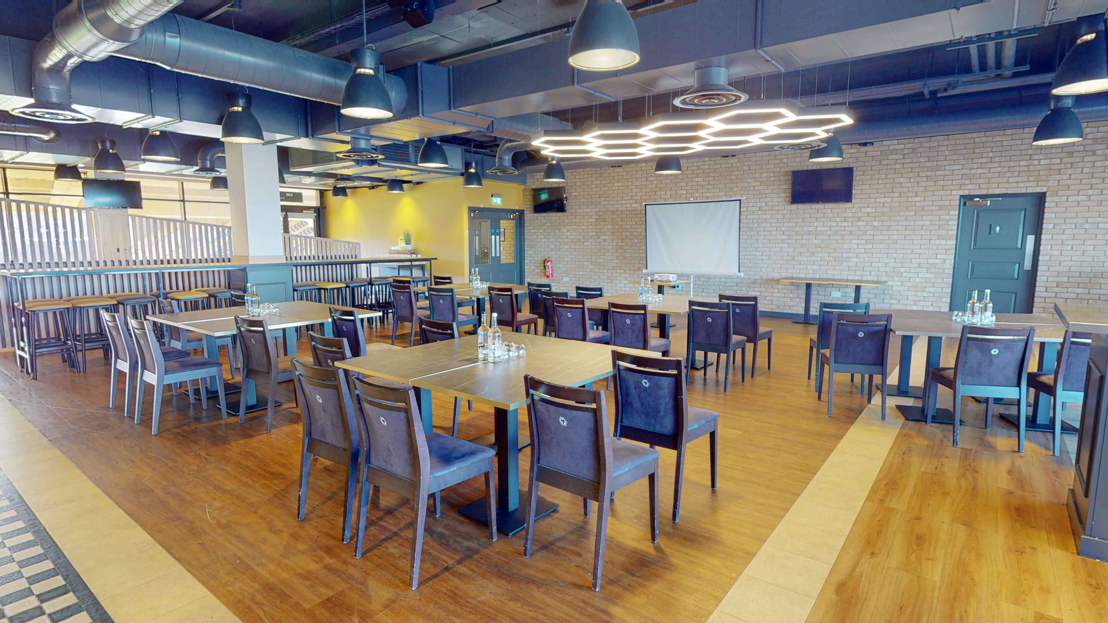Spacious function room with wooden tables, upholstered chairs and a projection screen.