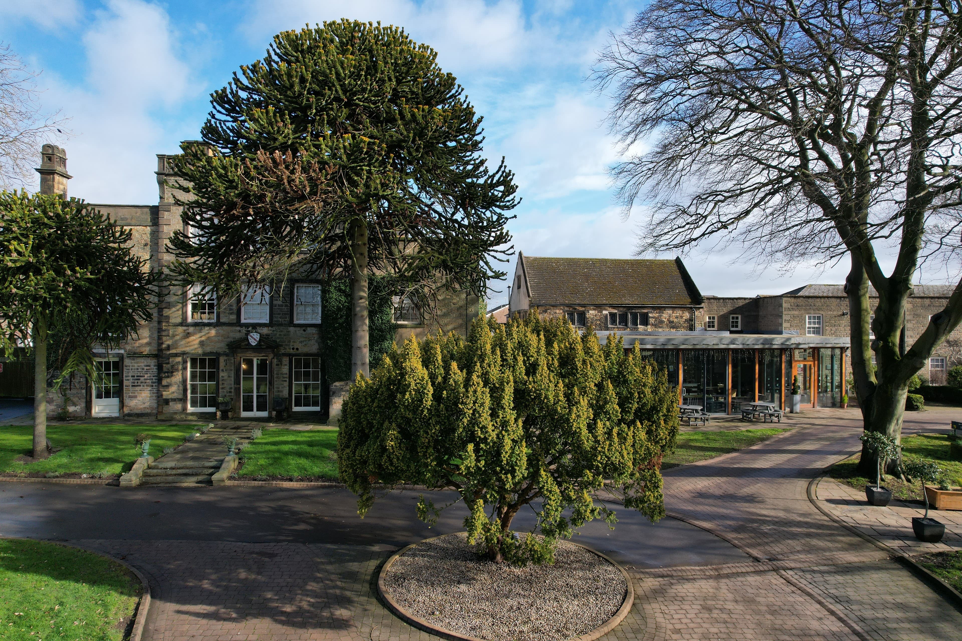 Exterior of Mosborough Hall Hotel showing stone facade, mature monkey puzzle trees and courtyard.