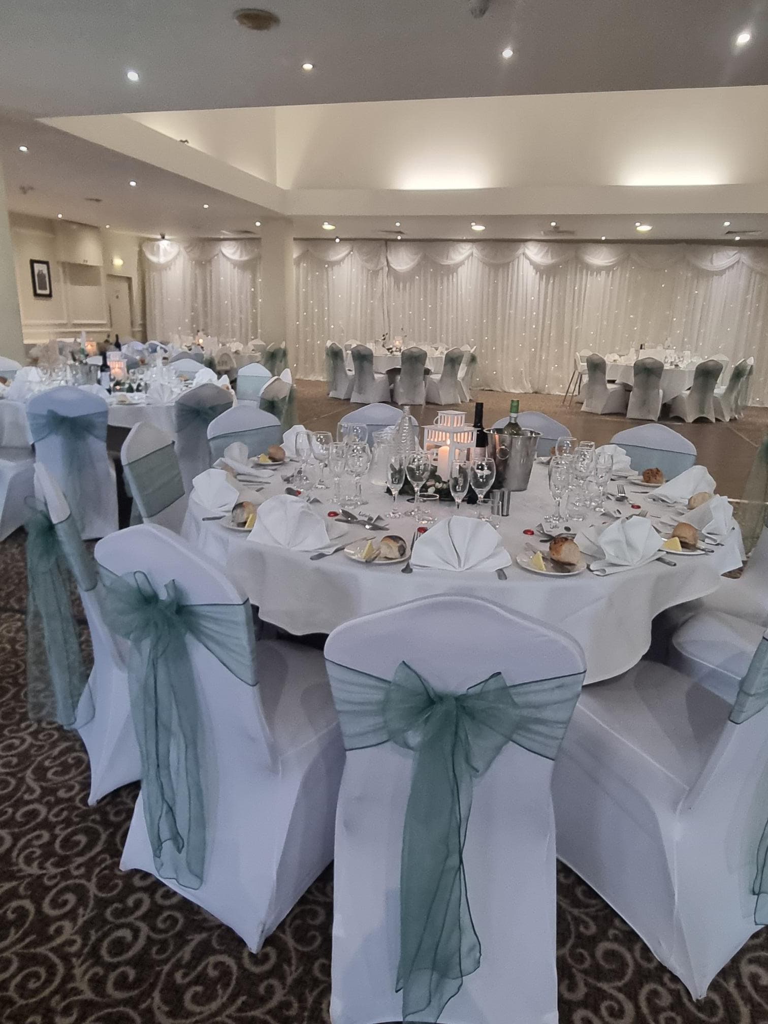 Banqueting room at Mosborough Hall Hotel laid for a formal dinner with white chair covers and sage green sashes.