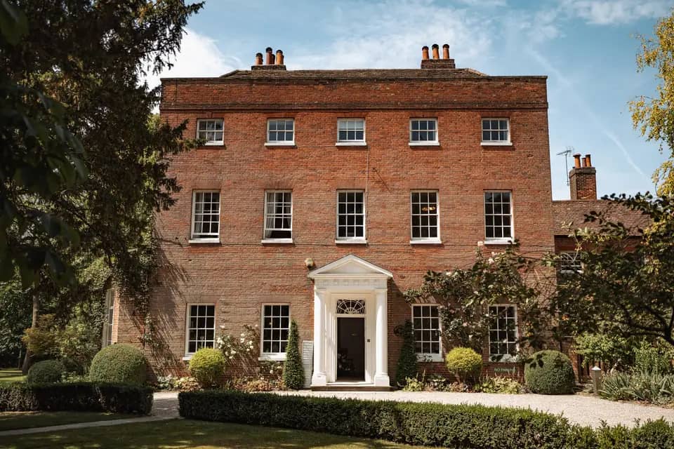 Red brick Georgian manor house with white portico entrance and manicured garden hedging