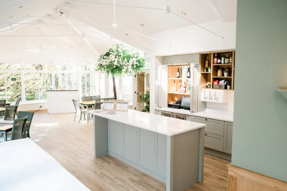 Light-filled conservatory dining room with a bar area and pale grey cabinetry.