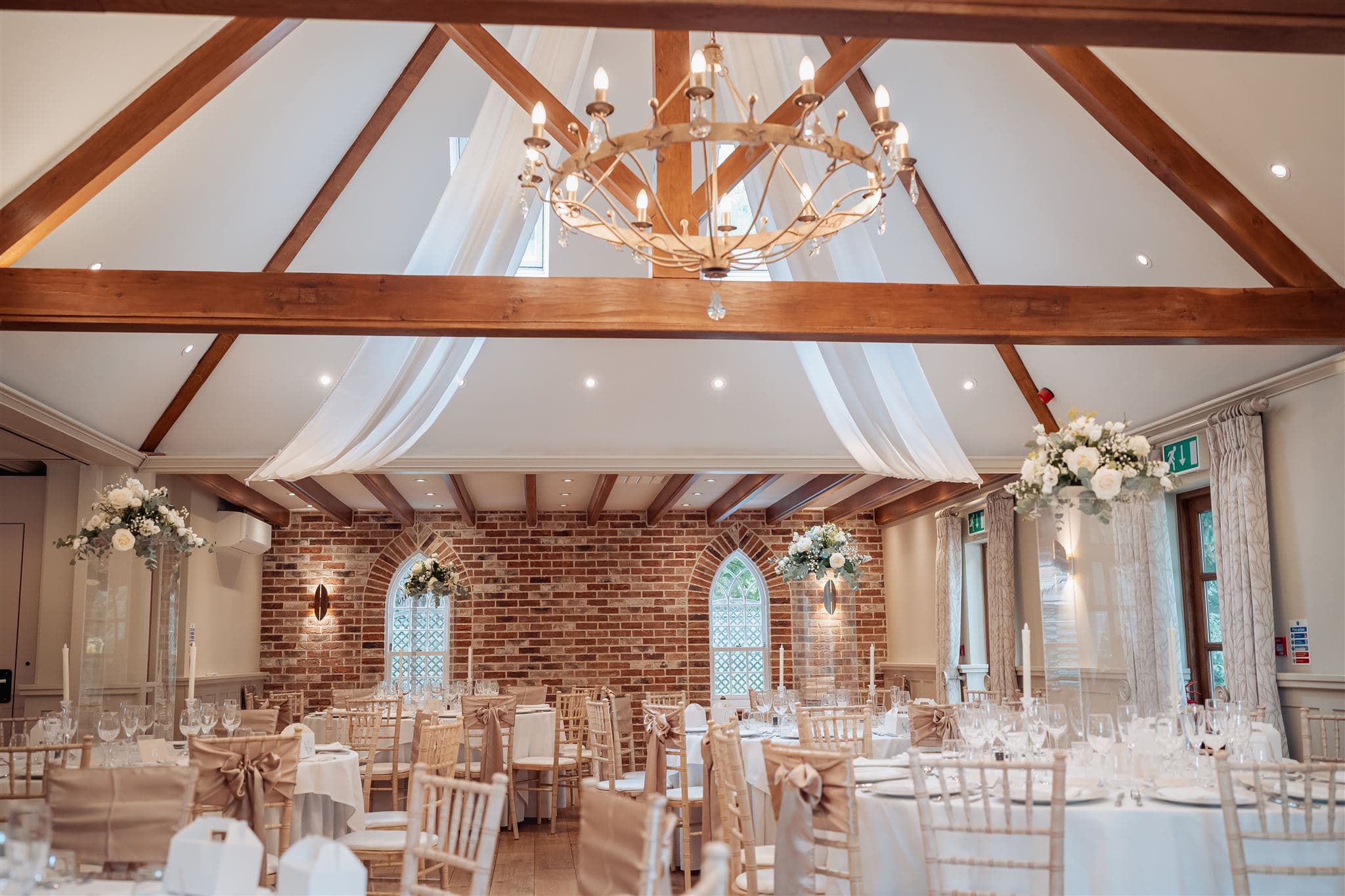 Dressed wedding reception room with exposed brick wall, timber beams and chandelier