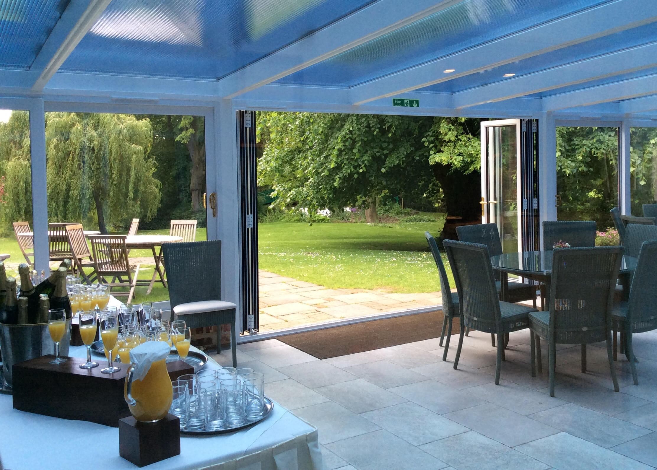 Glass conservatory with open bifold doors leading to a landscaped garden, drinks laid out on table.
