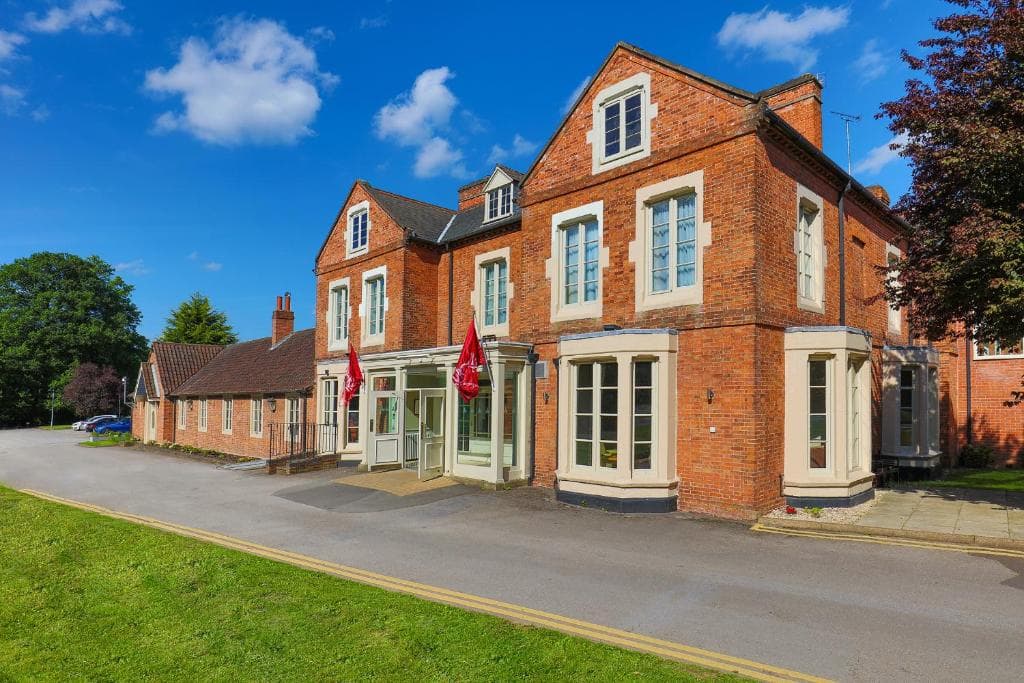 Red brick Victorian hotel exterior with two red flags and manicured lawns on a sunny day.