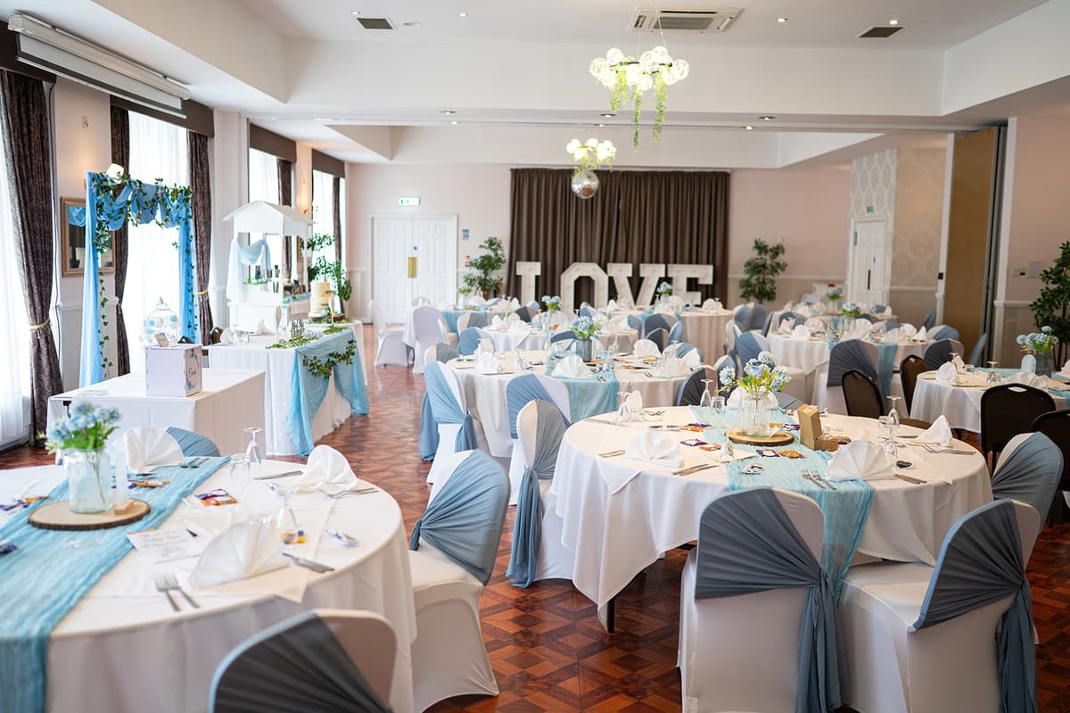 Wedding reception room with round tables, blue sashes and illuminated LOVE letters.
