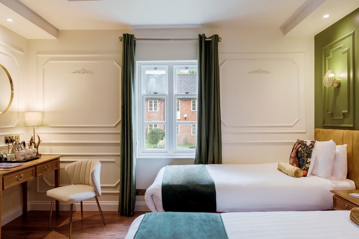 Twin bedroom with white panelled walls, green curtains and a wooden dressing table.