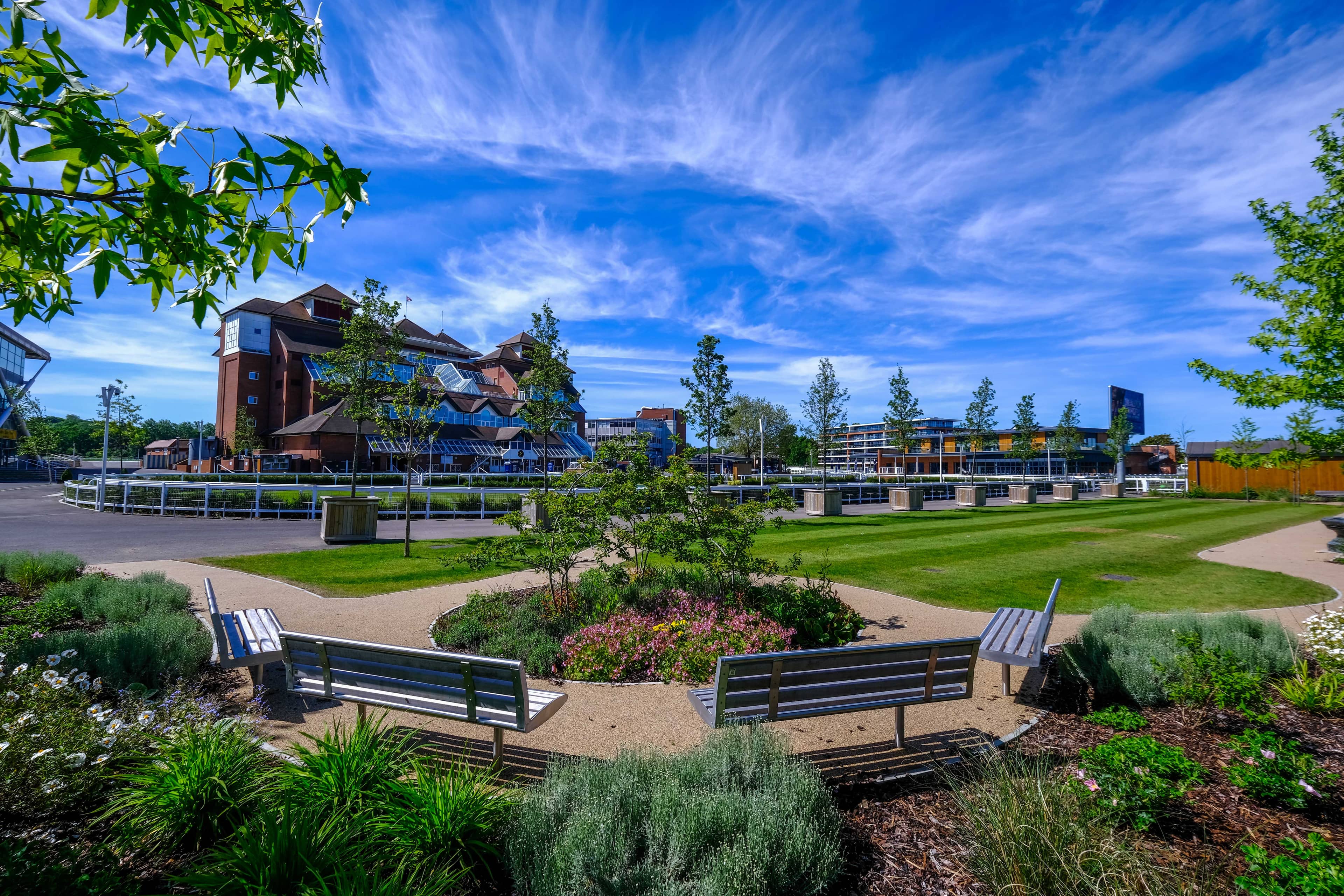 Landscaped gardens with benches and flower beds at Newbury Racecourse on a sunny day.