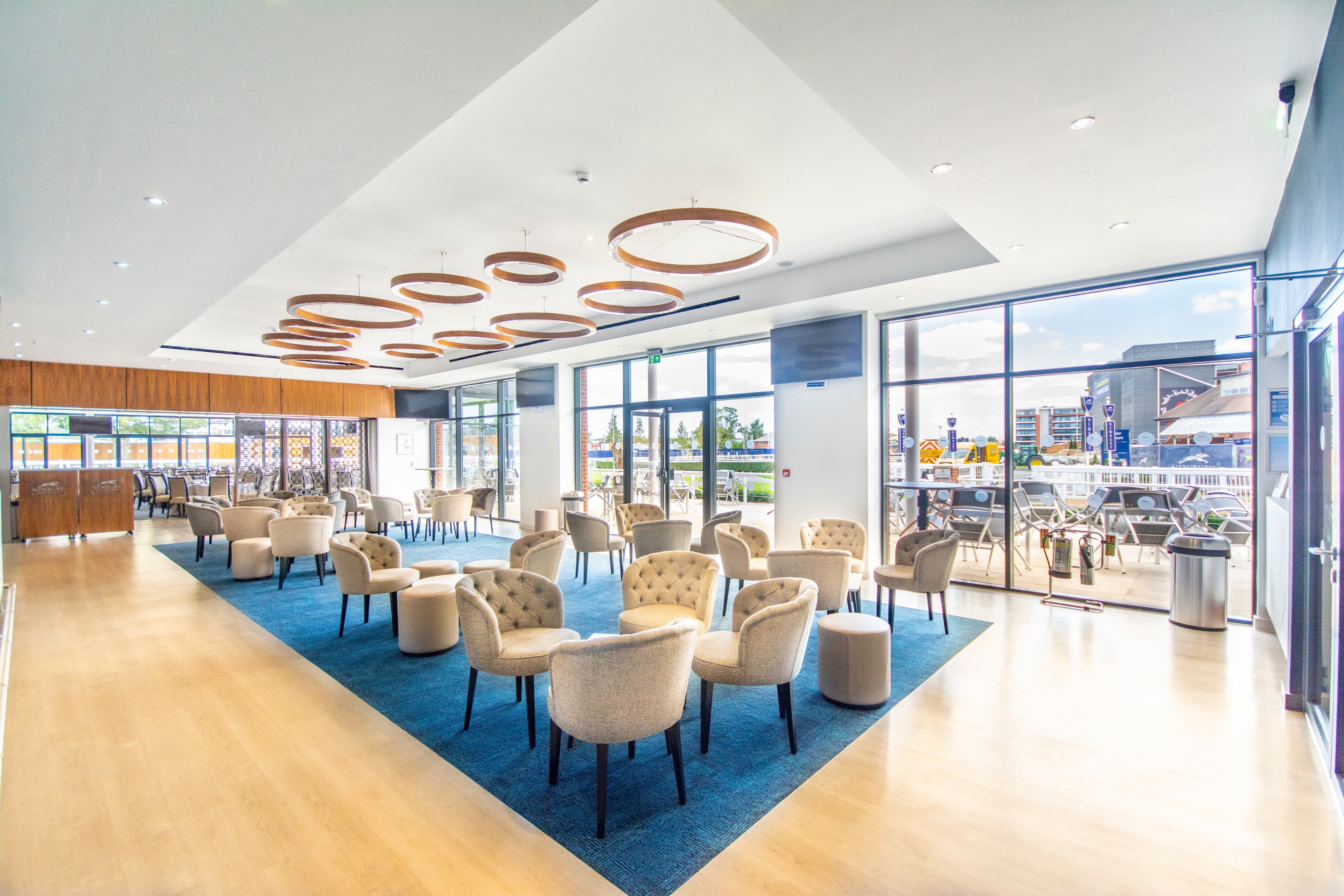 Bright hospitality lounge at Newbury Racecourse with cream tub chairs and circular pendant lights.