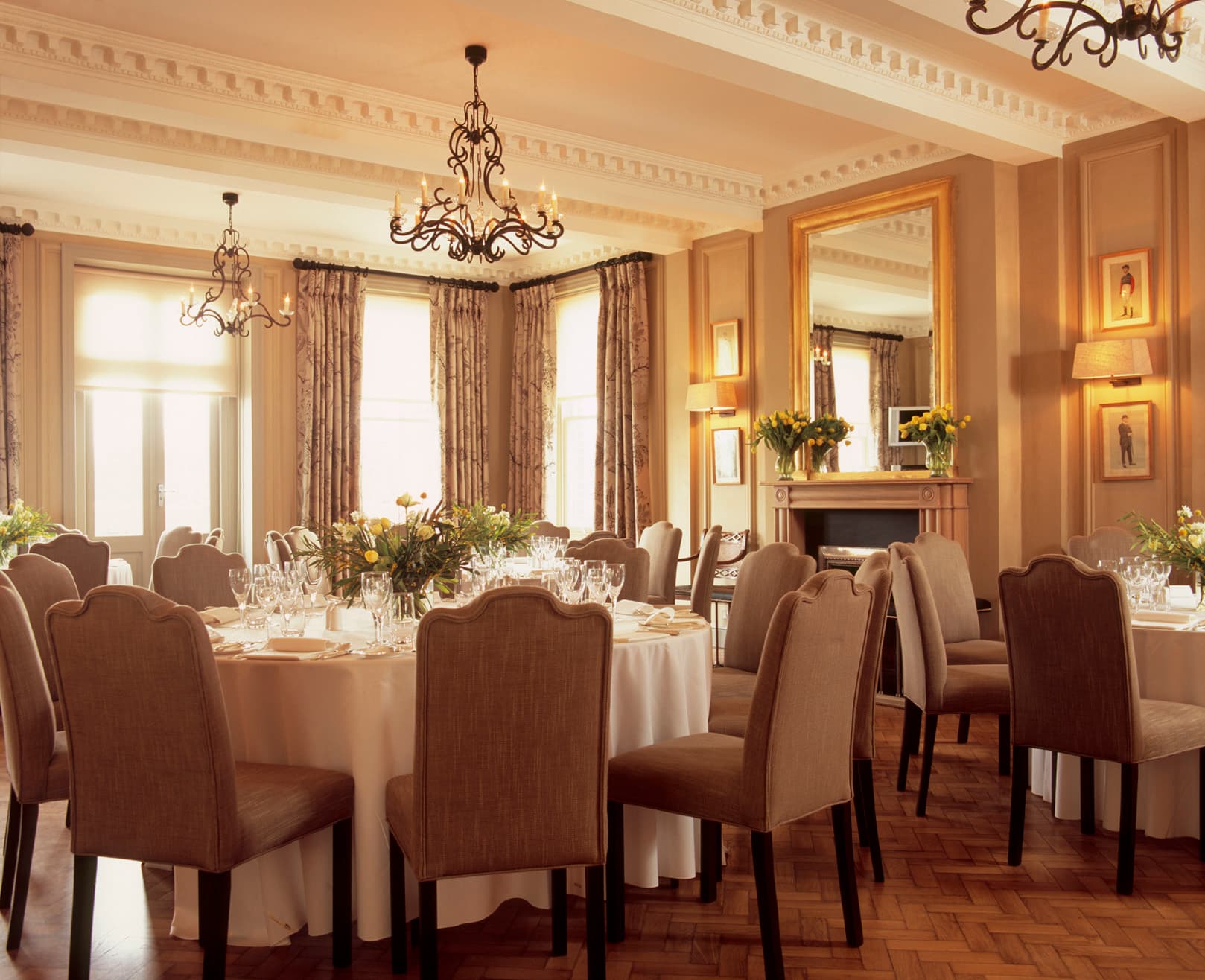 Elegant private dining room with round tables, chandeliers and a gilt mirror at Newbury Racecourse.