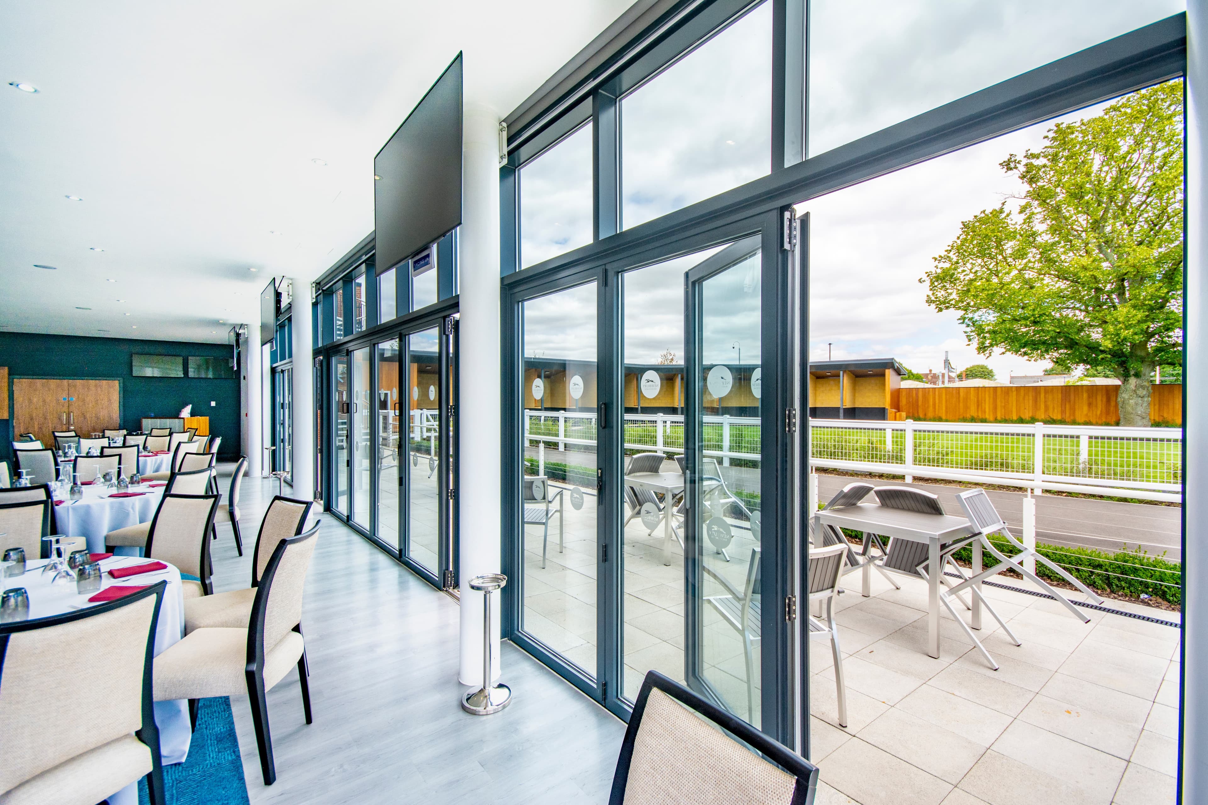 Dining room with white-clothed tables opening onto a terrace overlooking the racecourse track.