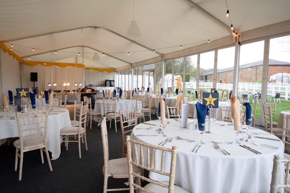 Marquee function room with round tables, chiavari chairs and a bar area overlooking the racecourse.