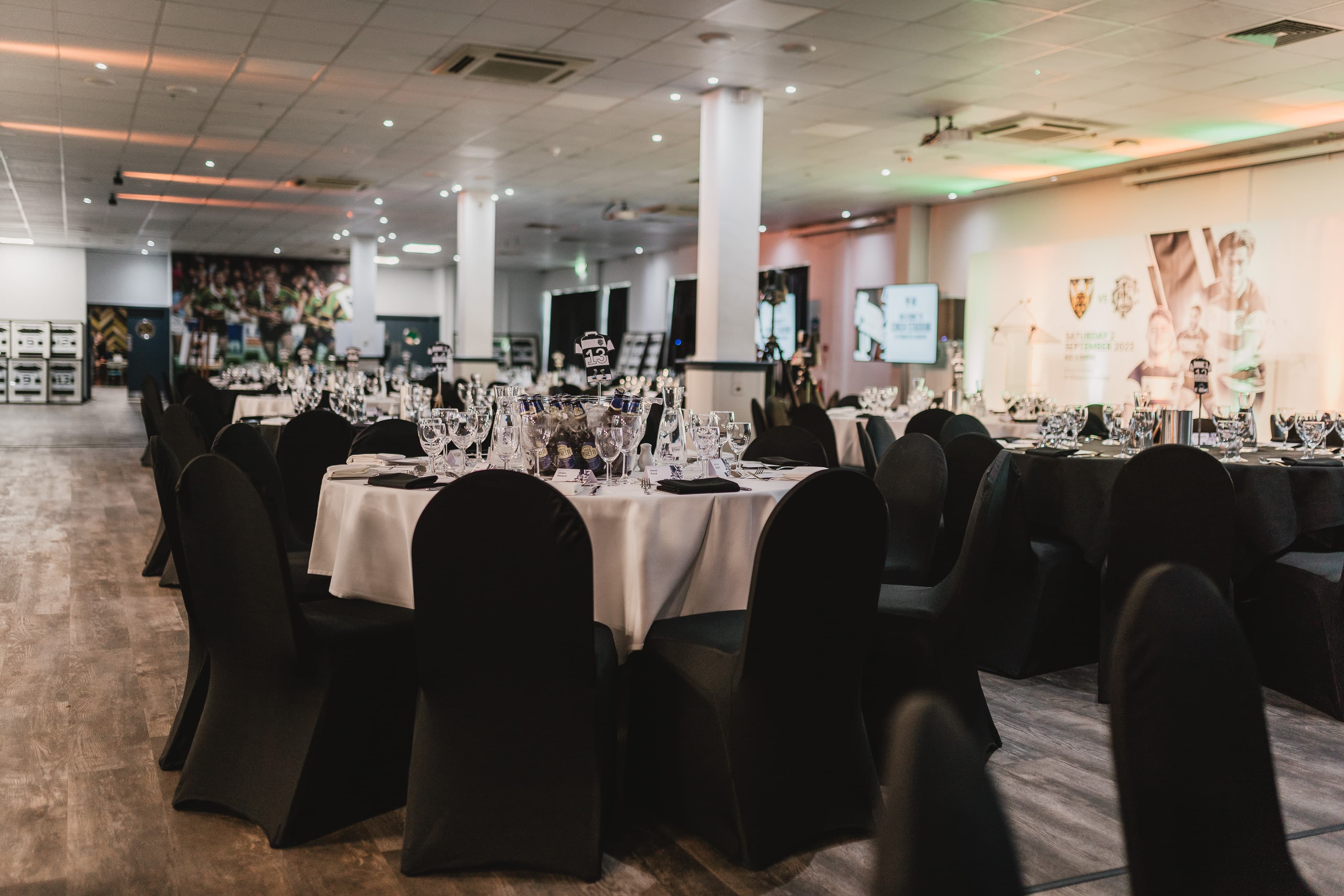 Banqueting room set with round tables, black chair covers and wine glasses.