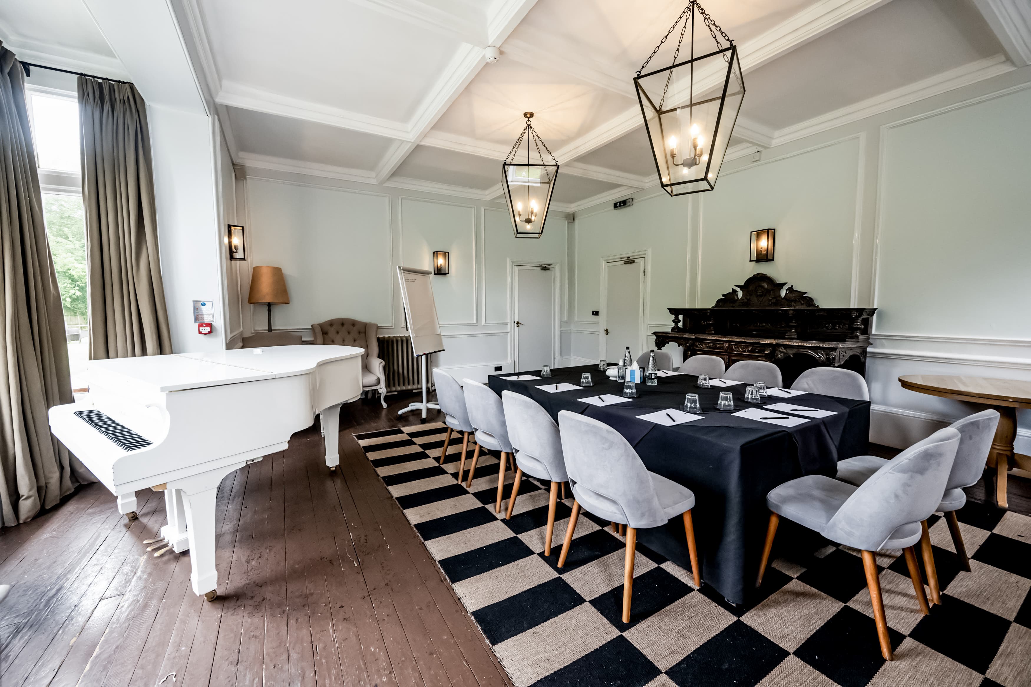 Meeting room with black draped table, grey chairs, white grand piano and ornate fireplace.