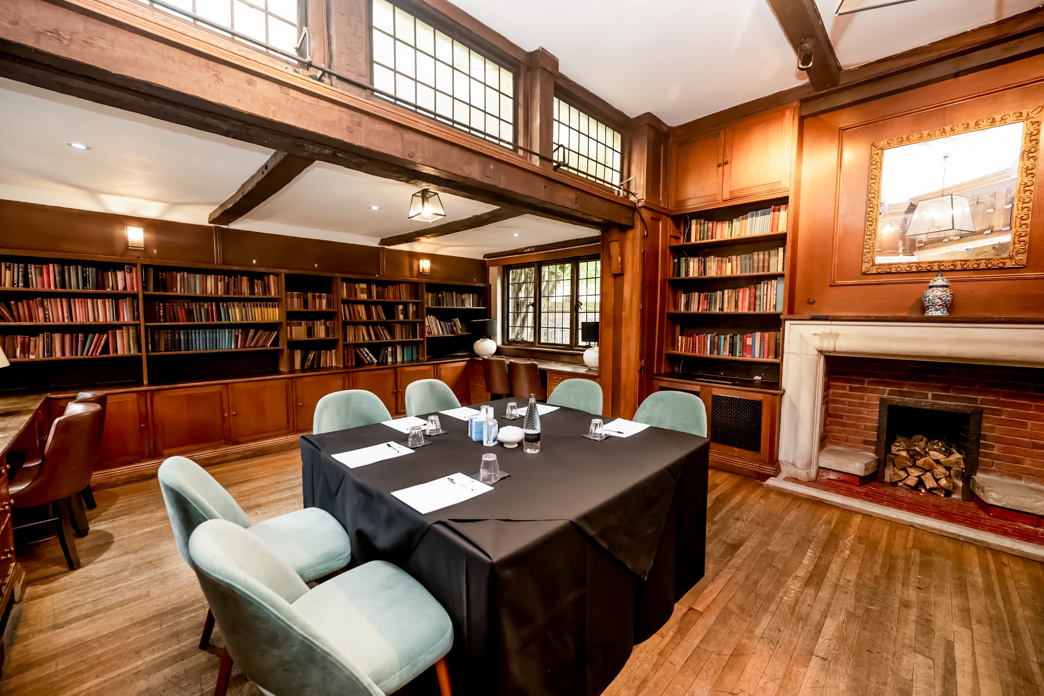 Wood-panelled library meeting room with black tablecloth, teal chairs and open fireplace.