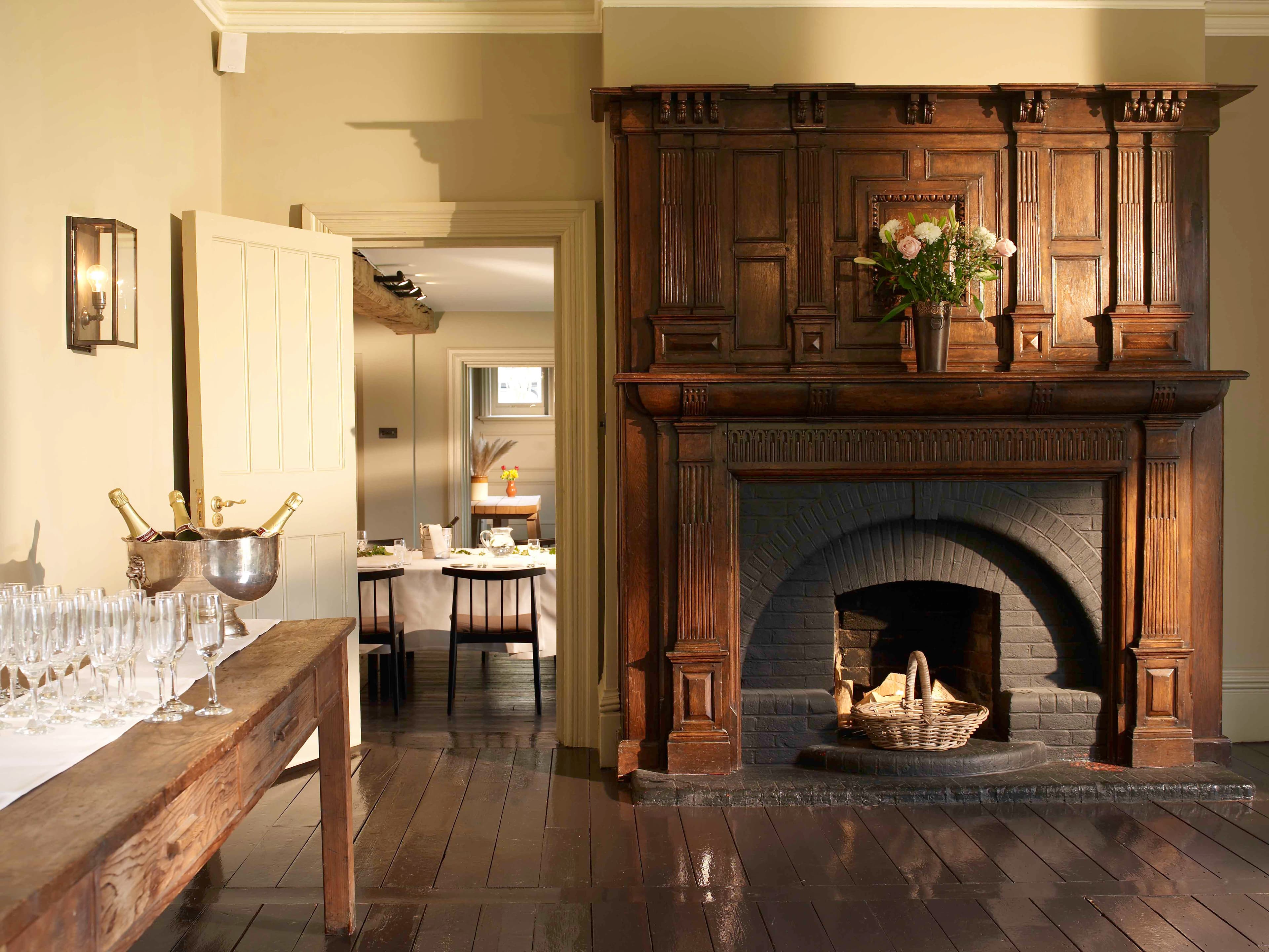 Grand carved oak fireplace with champagne glasses and log basket in a reception room.