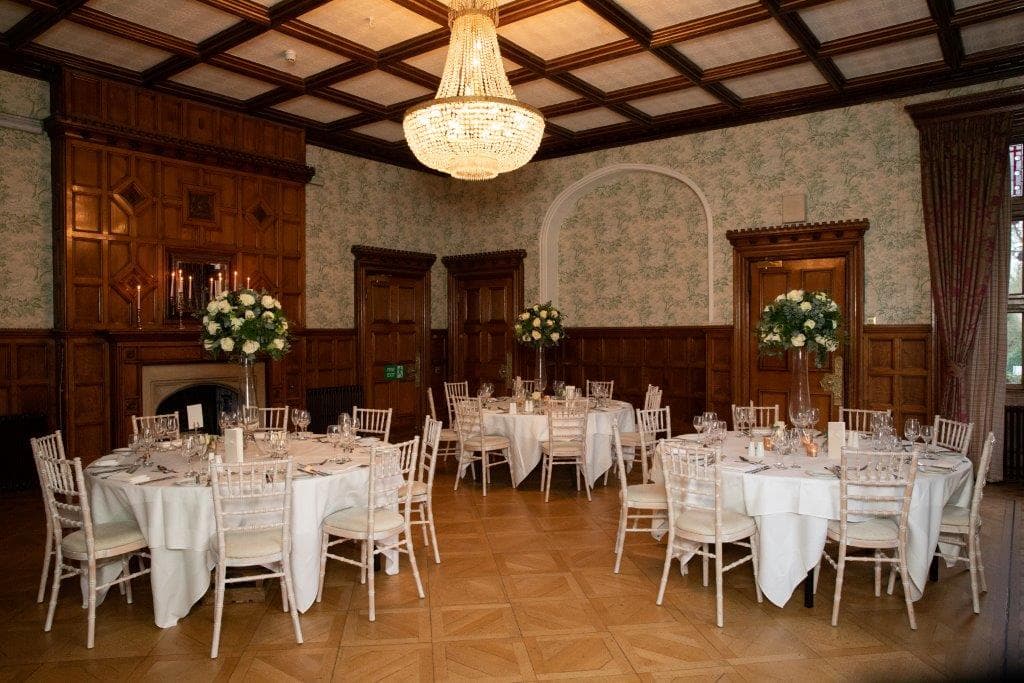 Pendley Manor Hotel function room with round tables, chiavari chairs and a crystal chandelier.
