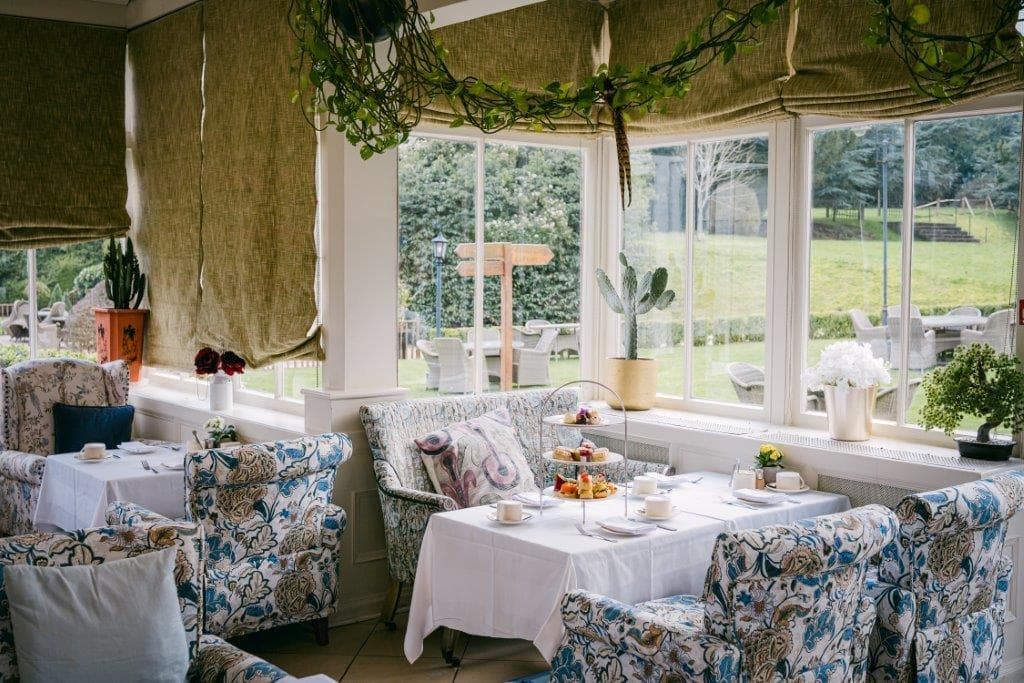 Light-filled conservatory dining room set for afternoon tea with floral armchairs and garden views.