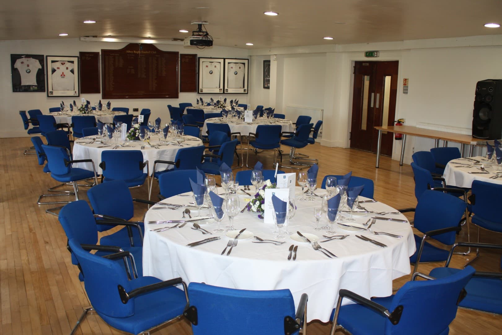 Function room at Reading Abbey RFC laid for a formal dinner with round tables and blue chairs.