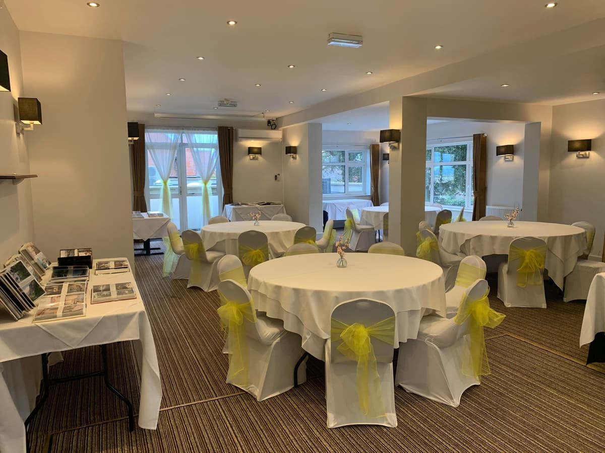 Function room at Riviera Hotel laid with round tables, white chair covers and yellow sashes.