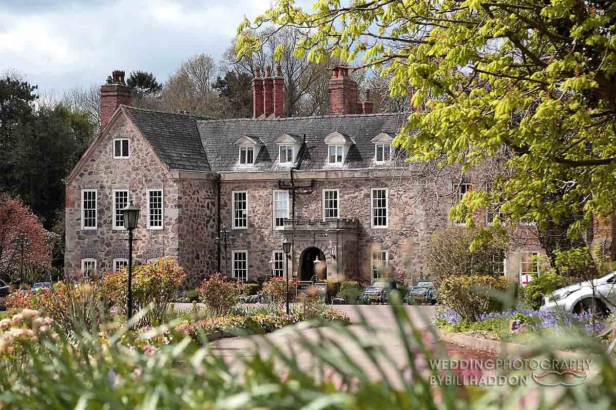 The stone exterior of Rothley Court Hotel seen through spring gardens and trees.