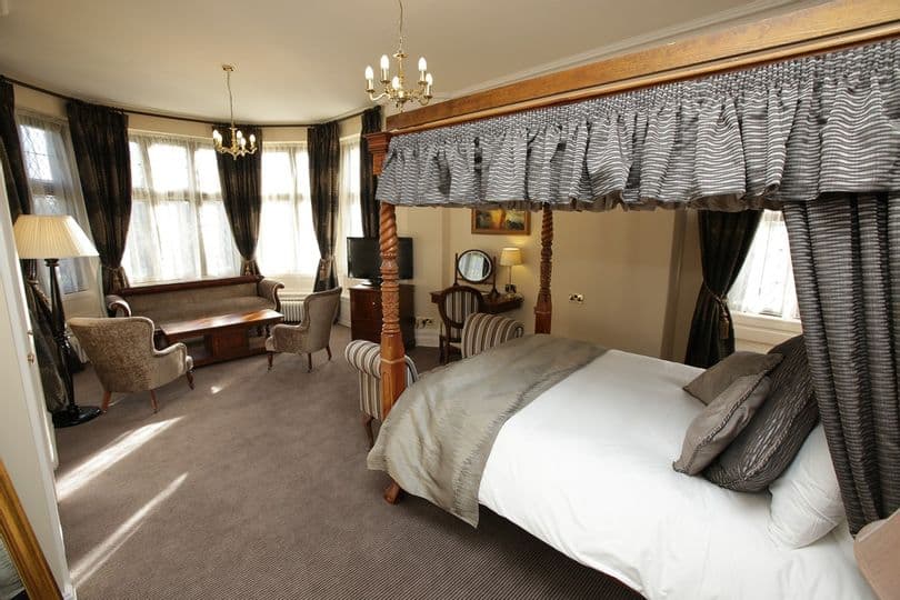 Four-poster bedroom with canopy drapes, seating area and bay windows at Rothley Court Hotel.