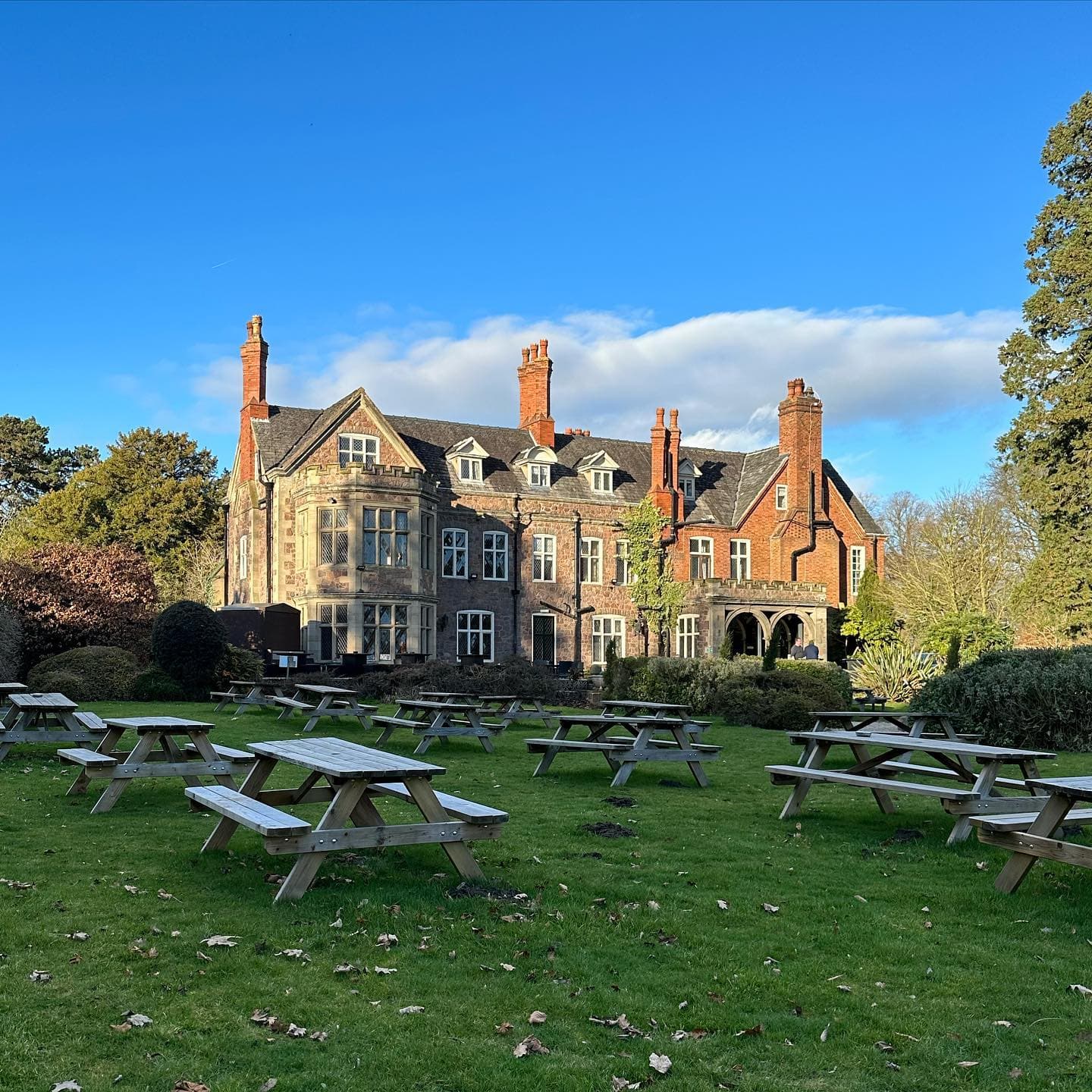 Rothley Court Hotel exterior with wooden picnic benches on a lawned garden under blue skies.