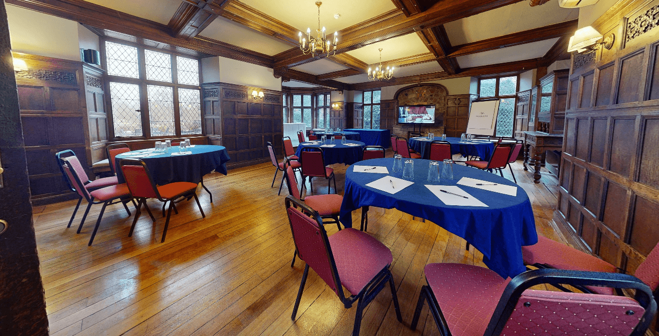 Panelled meeting room with round tables, red chairs and leaded windows at Rothley Court Hotel.