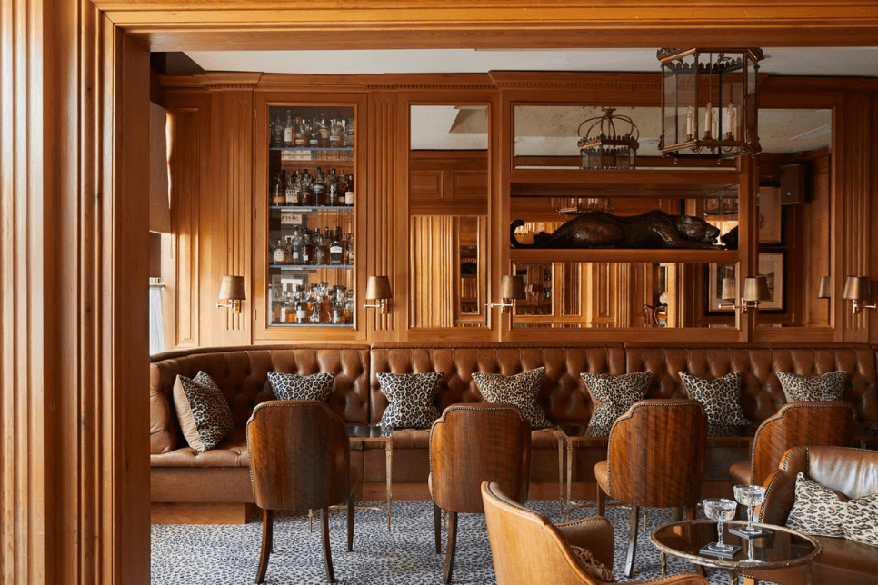 Wood-panelled hotel bar with brown leather banquettes, leopard print cushions and a spirits cabinet.
