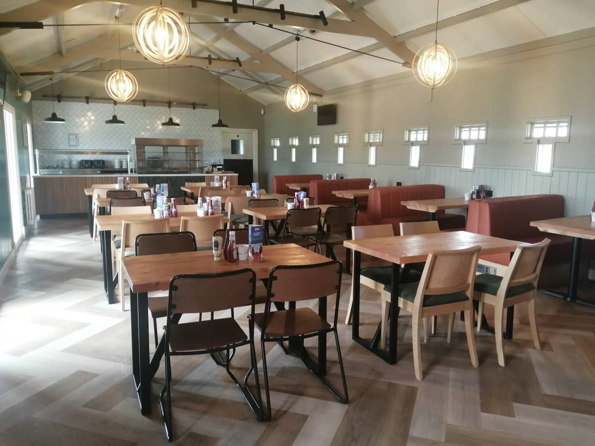 Bright dining room with wooden tables, mixed chairs and red booth seating at Southwell Racecourse.