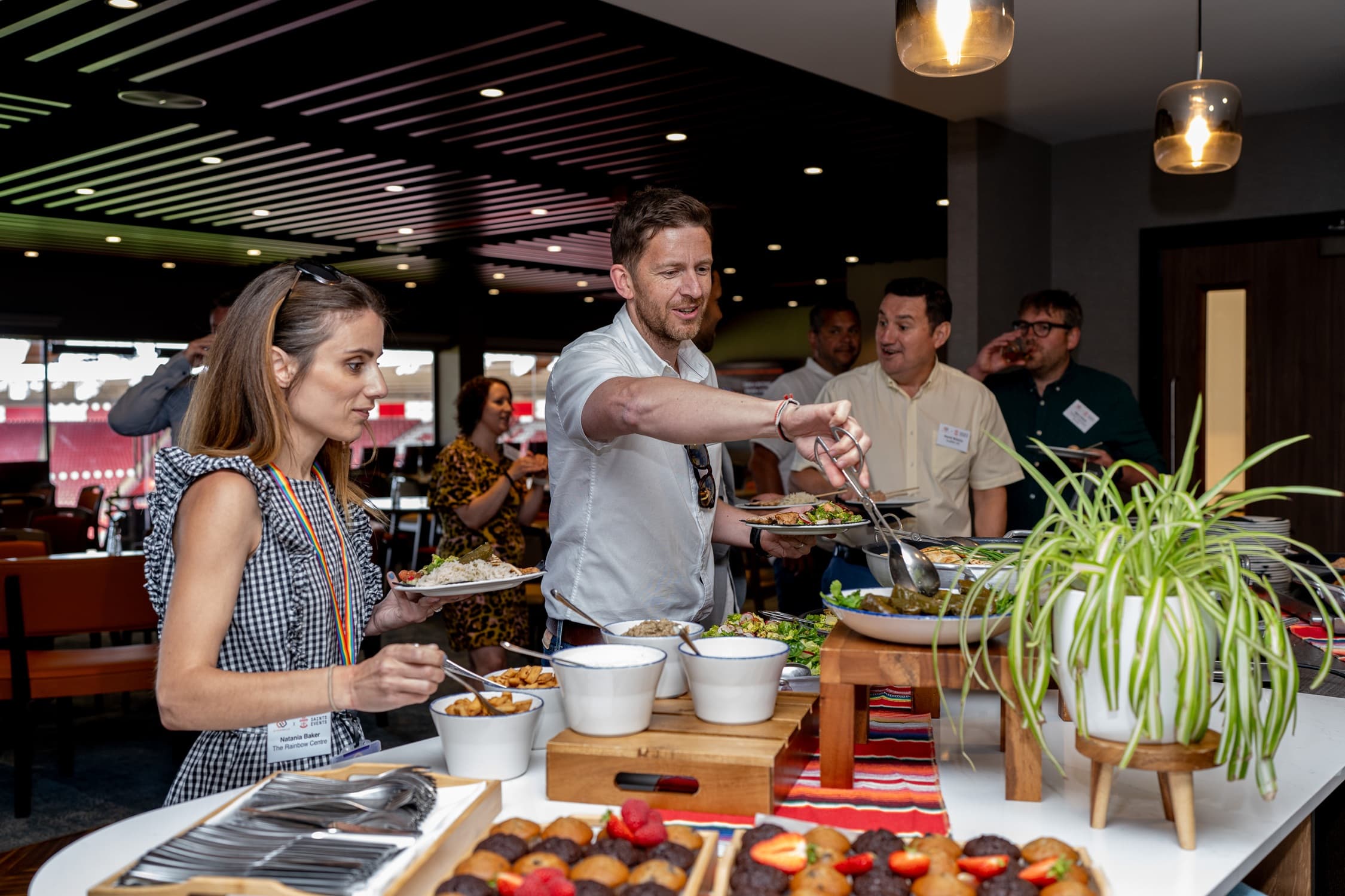 Guests helping themselves to a buffet spread in a modern stadium function room.