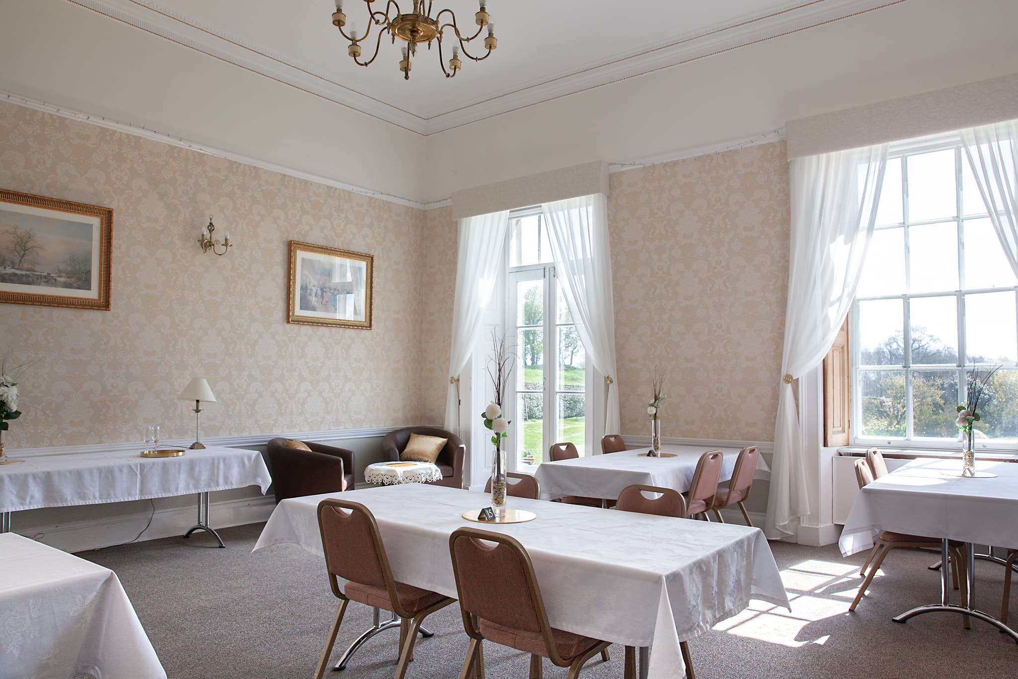 Strelley Hall dining room with white-clothed tables, damask walls and a brass chandelier.