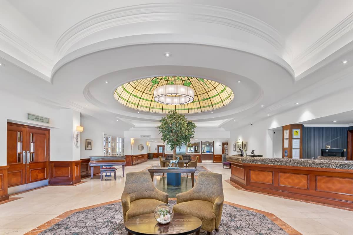 Hotel lobby with stained glass dome ceiling, reception desk and seating area.