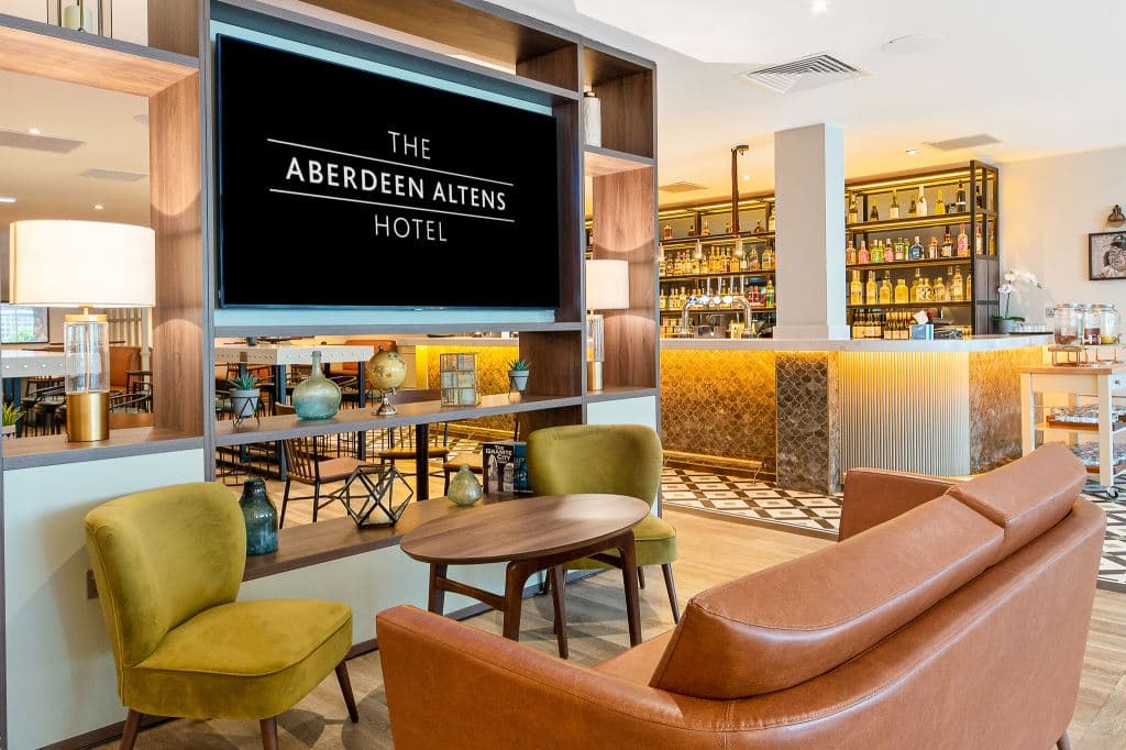 Bar lounge area with tan leather sofa, olive green chairs and well-stocked back bar.