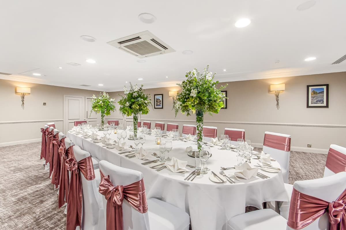 Private dining room laid for a formal event with tall floral centrepieces and pink satin chair sashes.