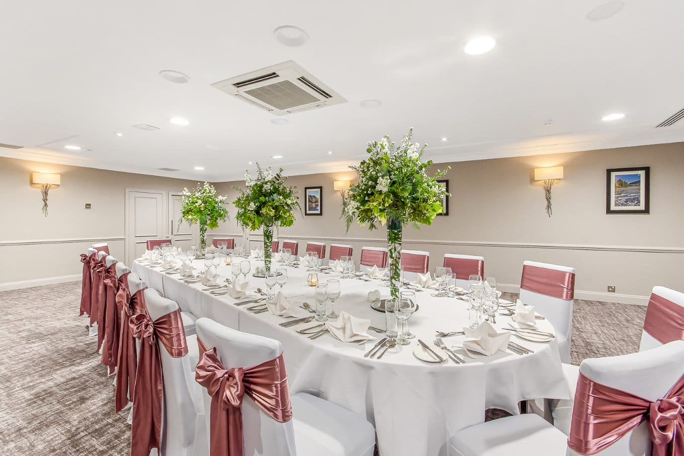 Private dining room laid for a formal event with tall floral centrepieces and pink satin chair sashes.