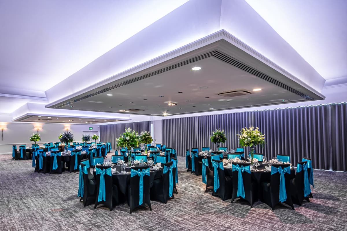 Banqueting room with round tables dressed in black linen and teal sash chairs