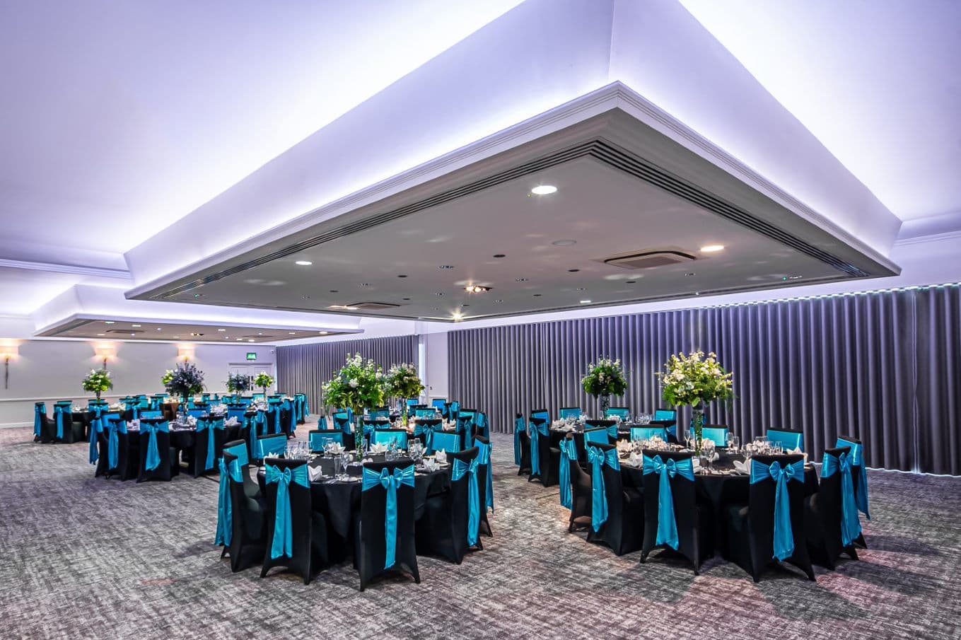 Banqueting room with round tables dressed in black linen and teal sash chairs